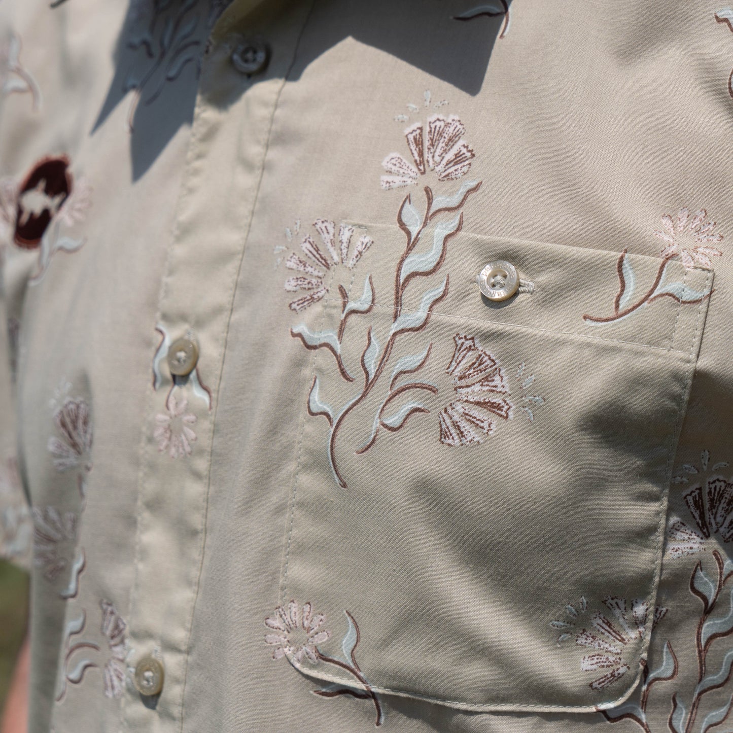 Close-up of the Patagonia M Brown Go To Shirt, a beige short-sleeve organic cotton button-up by Patagonia, featuring floral embroidery in light pink and brown, a front pocket, and several buttons.