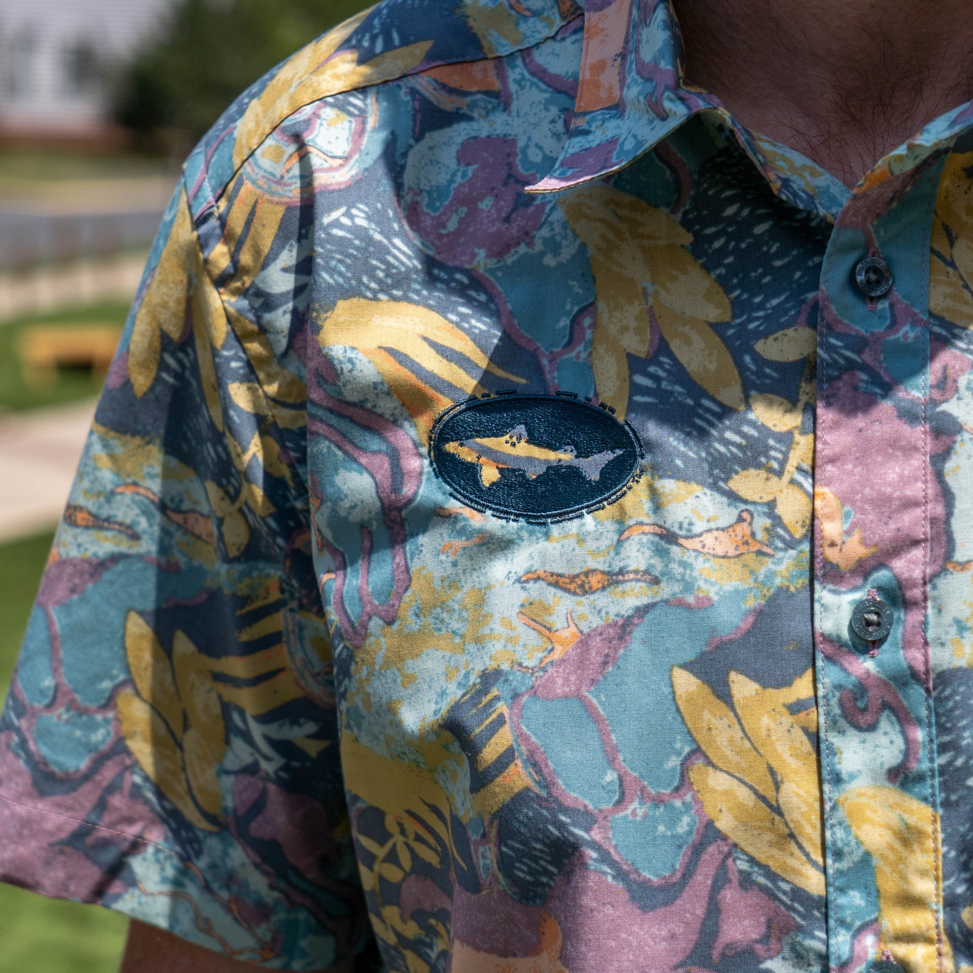 A person stands outdoors in sunlight wearing a Patagonia M Floral Pattern Go To Shirt, a lightweight, patterned button-up from Patagonia.
