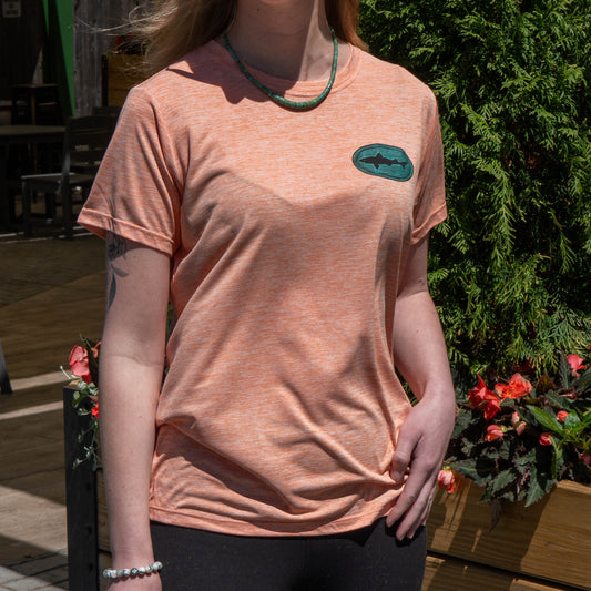 Patagonia women’s peach Cap Cool Daily shirt with a blue-green Dogfish Head shark logo, lightweight breathable performance t-shirt worn outdoors