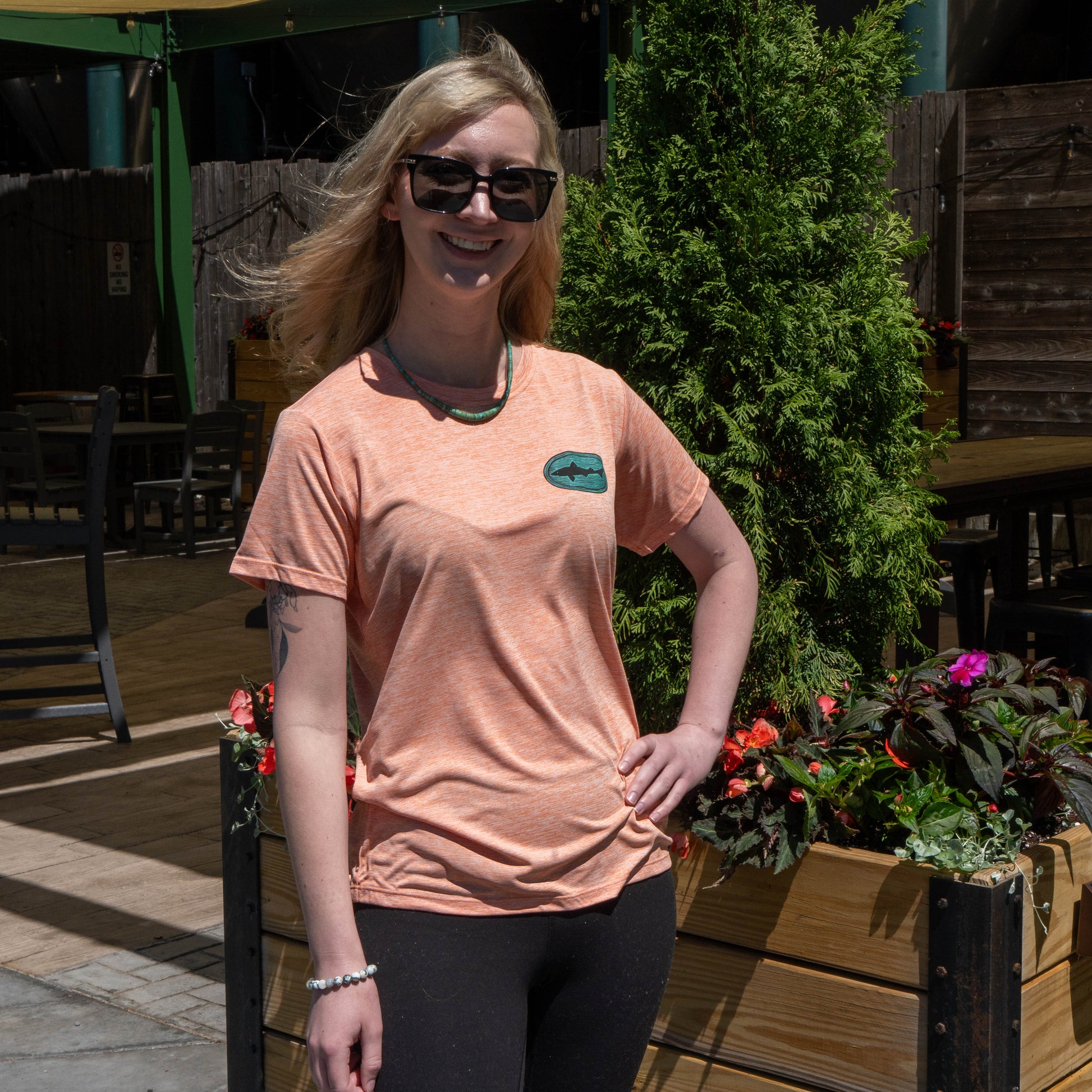 Patagonia women’s peach Cap Cool Daily shirt with blue-green Dogfish Head logo worn outdoors, lightweight summer performance t-shirt