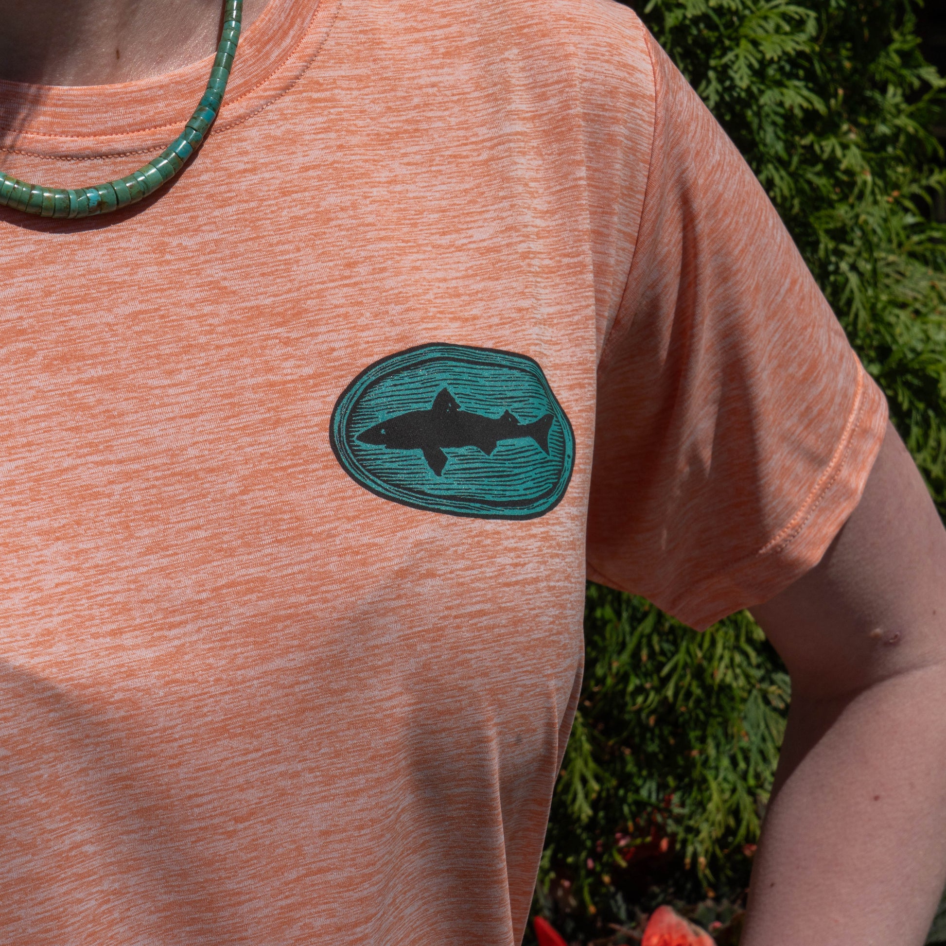 Close-up of Patagonia women’s peach Cap Cool Daily shirt featuring Dogfish Head woodgrain logo graphic in blue-green