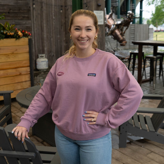 Patagonia x Dogfish Head purple crewneck sweatshirt featuring embroidered shark logo, worn casually on outdoor patio