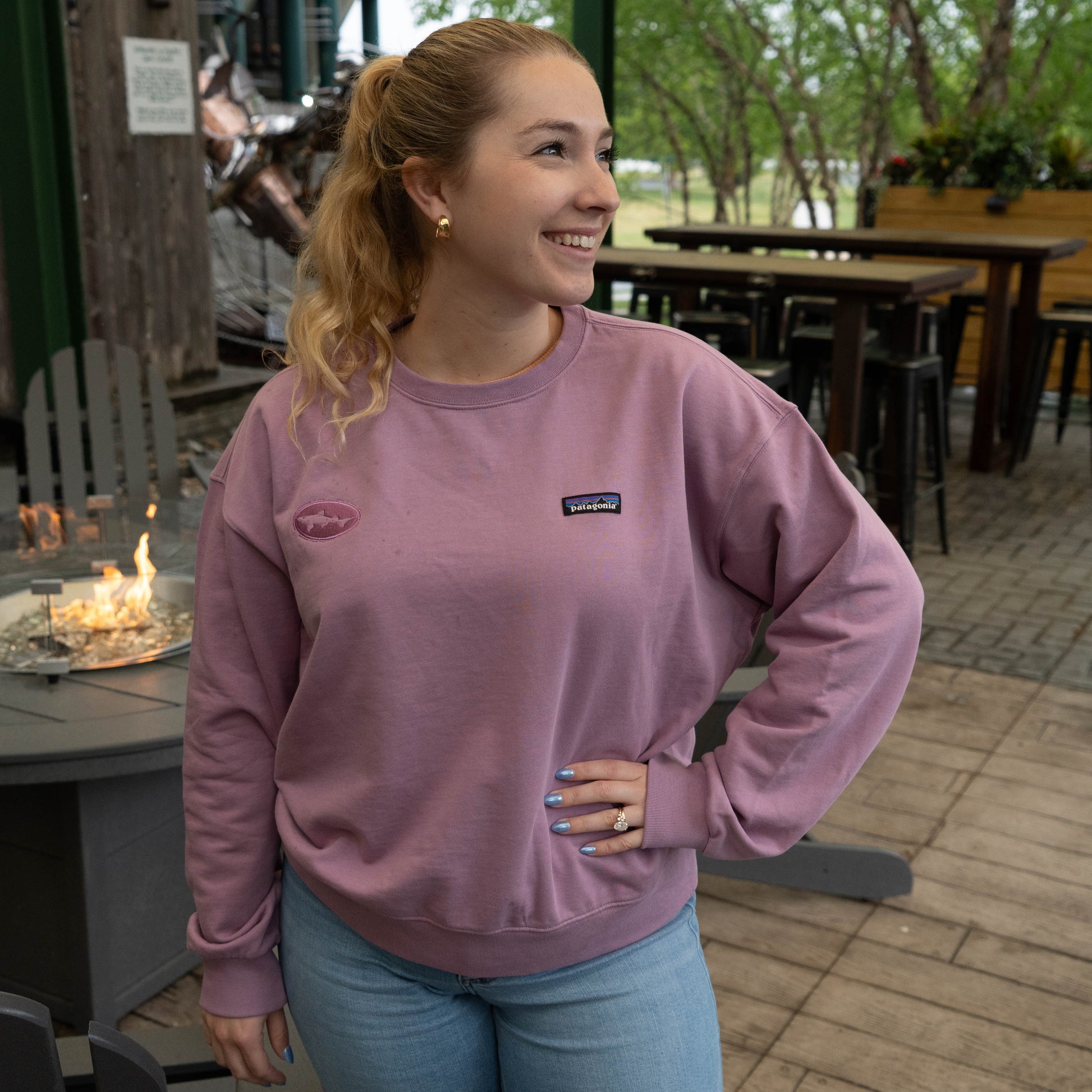 Side view of Patagonia Dogfish Head purple crew sweatshirt with logo patch, styled on outdoor brewery patio near fire pit