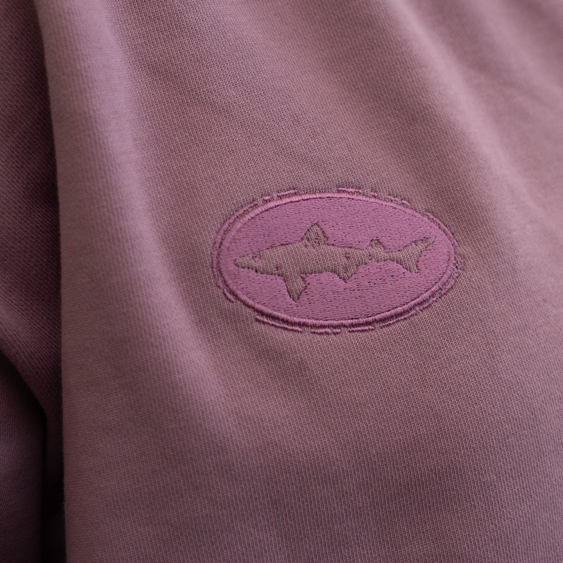 Close-up of purple embroidered dogfish logo on the sleeve of a matching purple crewneck sweatshirt