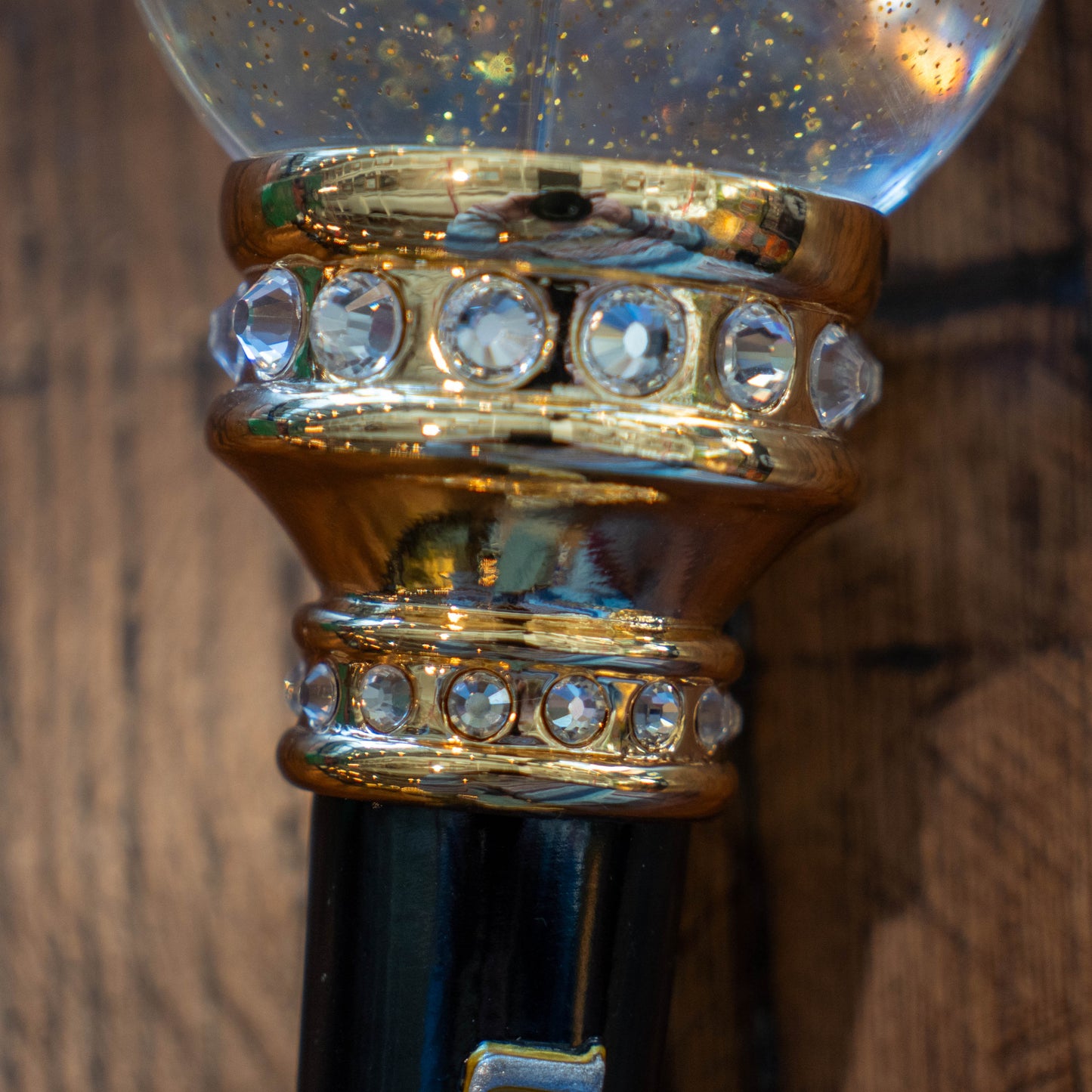 Close-up of the OG Uber Tap Handle by Taphandles Inc., a limited edition collectible featuring a gold band with clear gemstones and a clear globe filled with gold glitter, set against a wooden background.