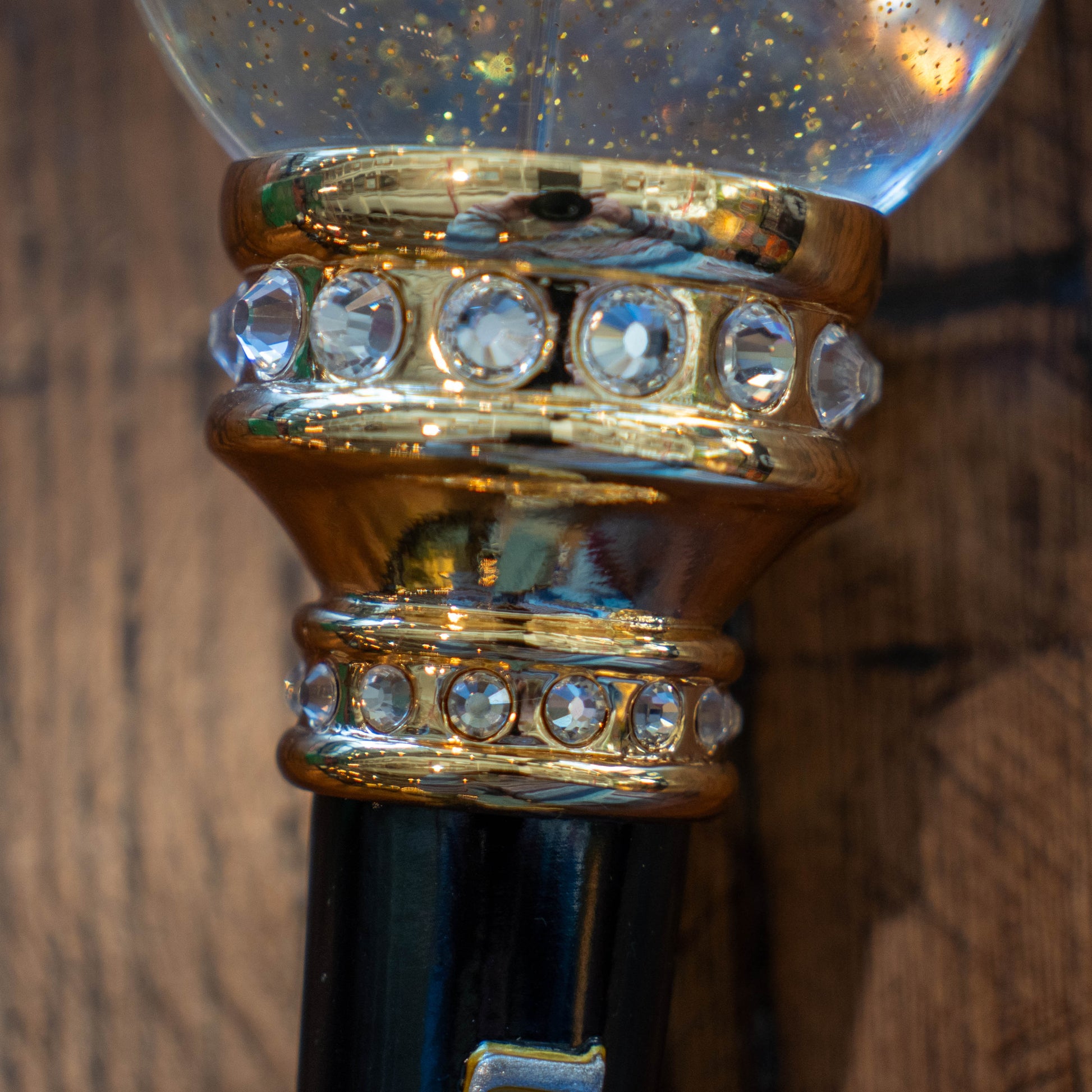 Close-up of the OG Uber Tap Handle by Taphandles Inc., a limited edition collectible featuring a gold band with clear gemstones and a clear globe filled with gold glitter, set against a wooden background.