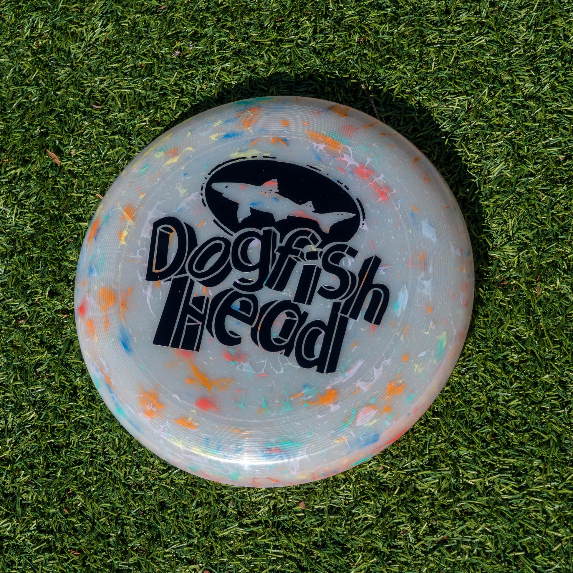 Grey frisbee with tie dye accents and a black Dogfish Head logo with "Dogfish Head" styled in 3-d block text laying on grass