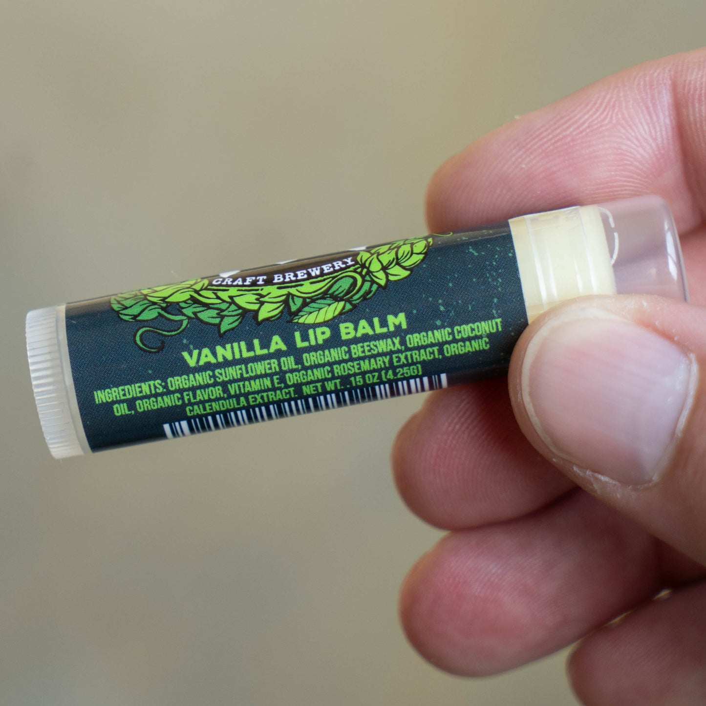 A hand holds a tube of Ecolips Vanilla Lip Balm, labeled with ingredients like organic sunflower oil, organic beeswax, organic coconut oil, organic flavor, vitamin E, rosemary extract, and calendula extract.