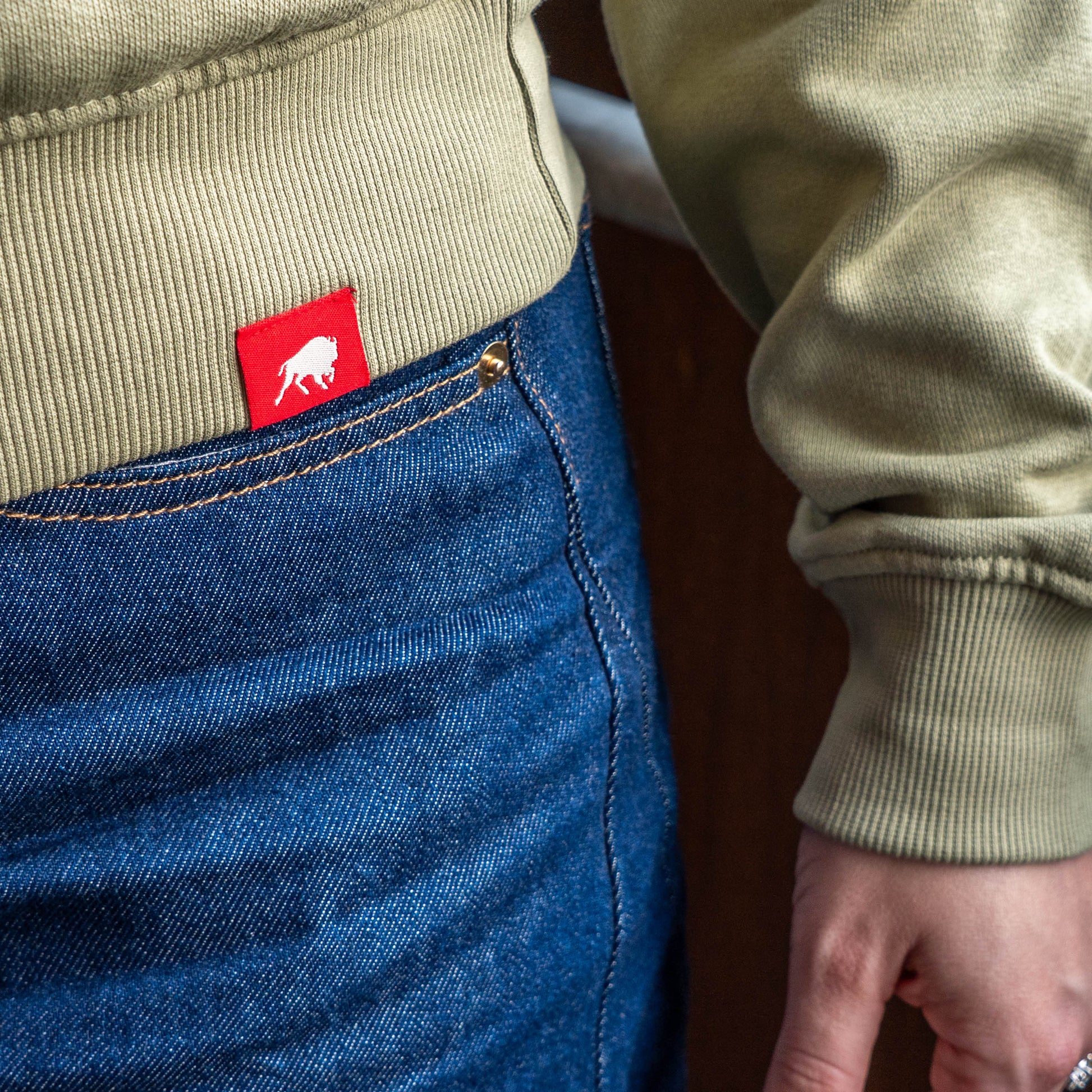Close up of red Sportiqe logo tag on the hemline of a mineral quarter zip pullover sweatshirt. 