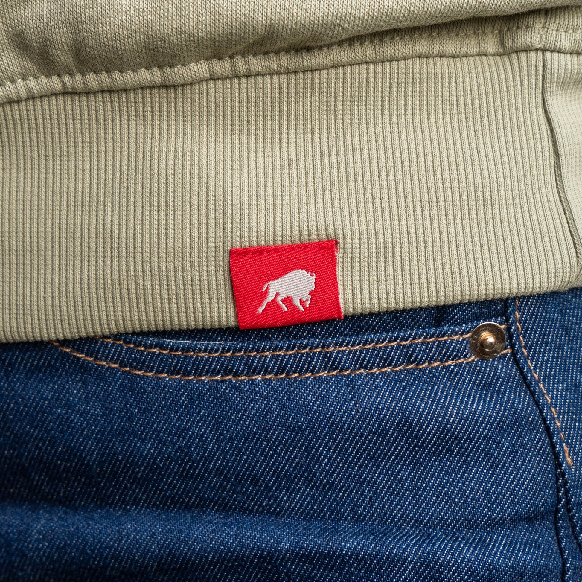 Close up of red Sportiqe logo tag on the hemline of a mineral quarter zip pullover sweatshirt. 