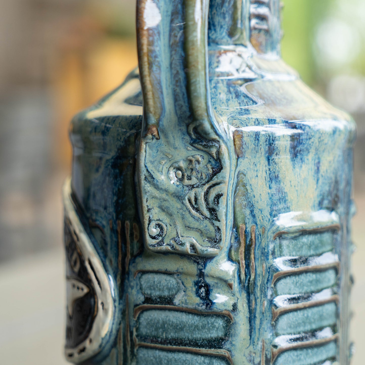 Close-up of the Romanick Pottery White Blue Green Ceramic Growler, showcasing hand-carved patterns and decorative details in blue, green, and beige glaze—expert ceramic craftsmanship in focus against a blurred background.