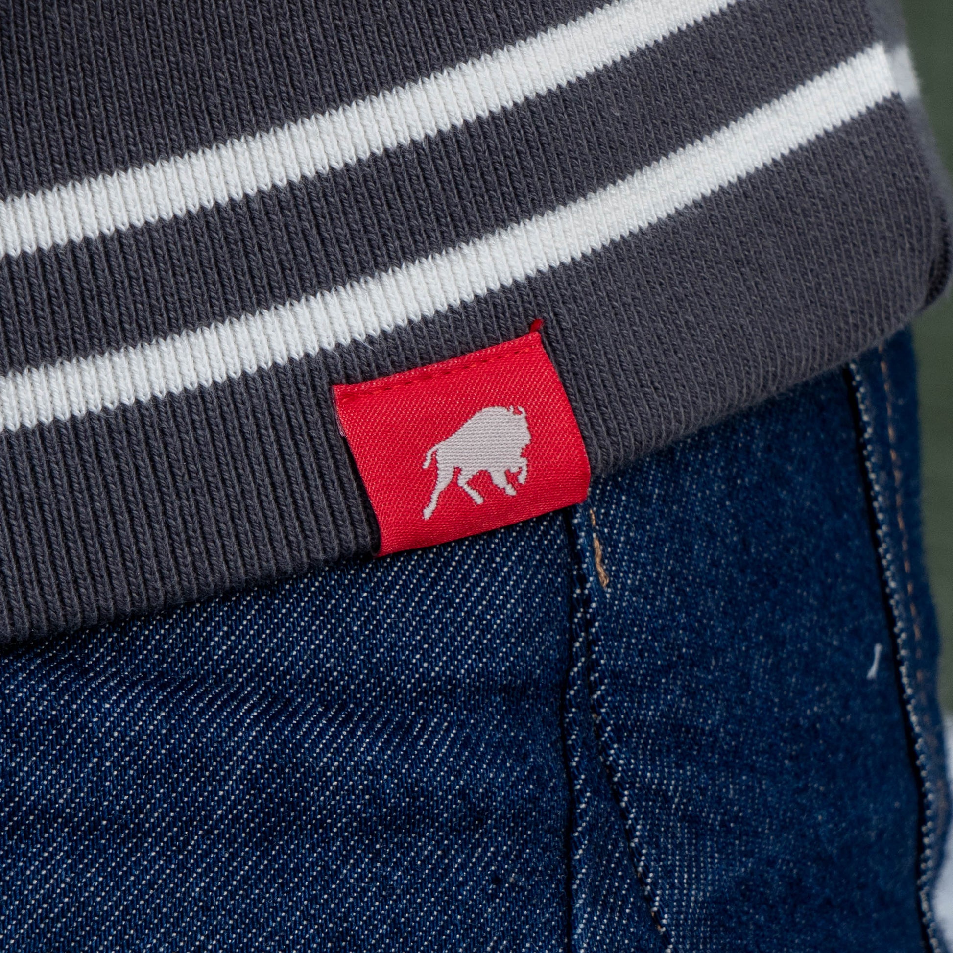 Close up of red Sportiqe logo tag on the hemline of the white crewneck sweatshirt