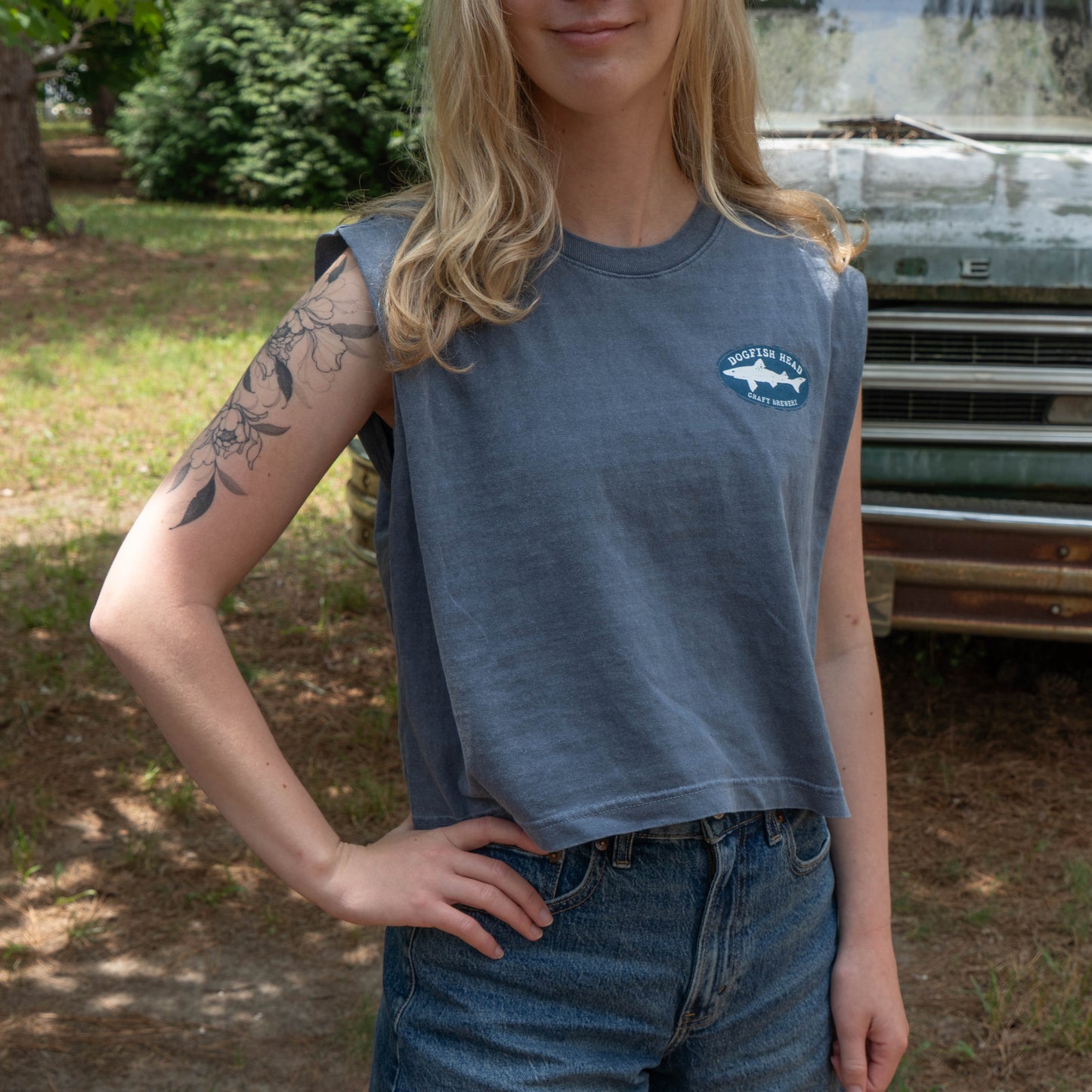 Person wearing a sleeveless blue shirt with a logo, standing outdoors.