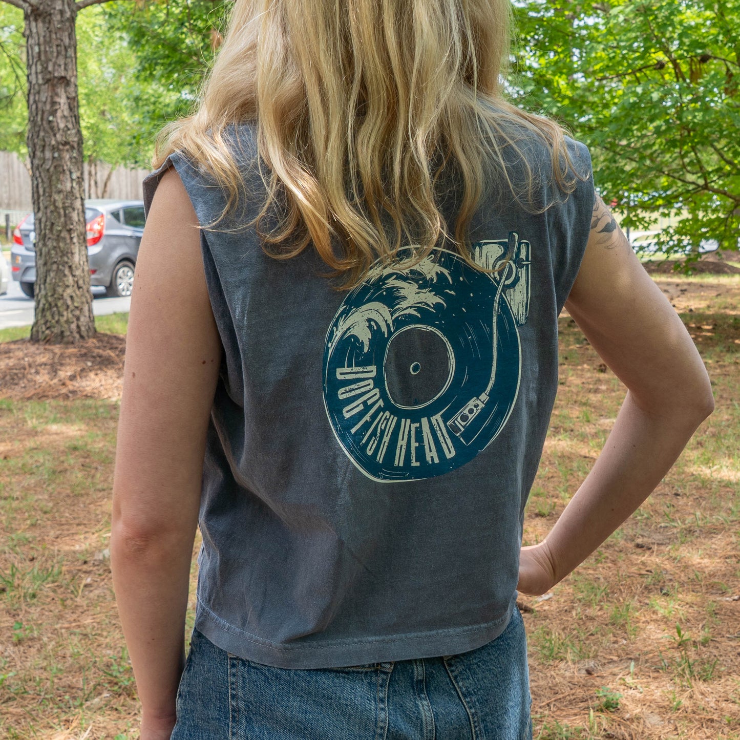 Person wearing a sleeveless denim shirt with a graphic design outdoors