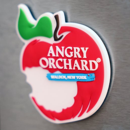 This magnet is shown displayed on a fridge. The magnet is the iconic Angry Orchard bitten red apple with writing "Angry Orchard" in white, and "Walden, New York" written under it on a blue background.