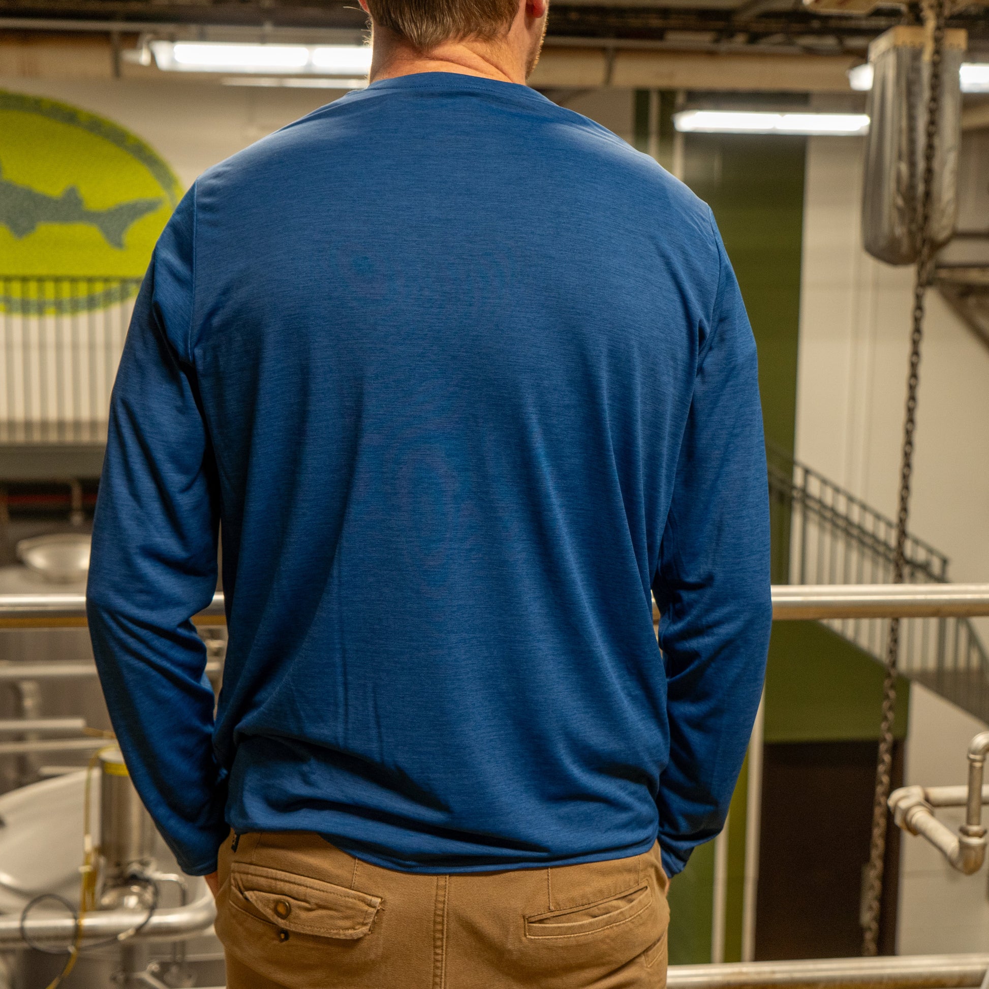 A person wearing a Patagonia M Blue Long Sleeve Runner stands with their back to the camera in an industrial setting with metal railings and equipment.