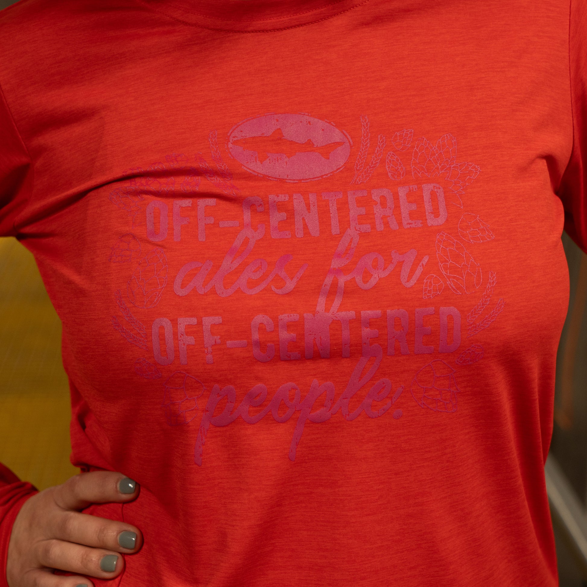 A person wearing the Patagonia W Red Long Sleeve Runner shirt with purple text reading "Off-centered ales for off-centered people." Only the torso is visible, and their hand rests on their hip.