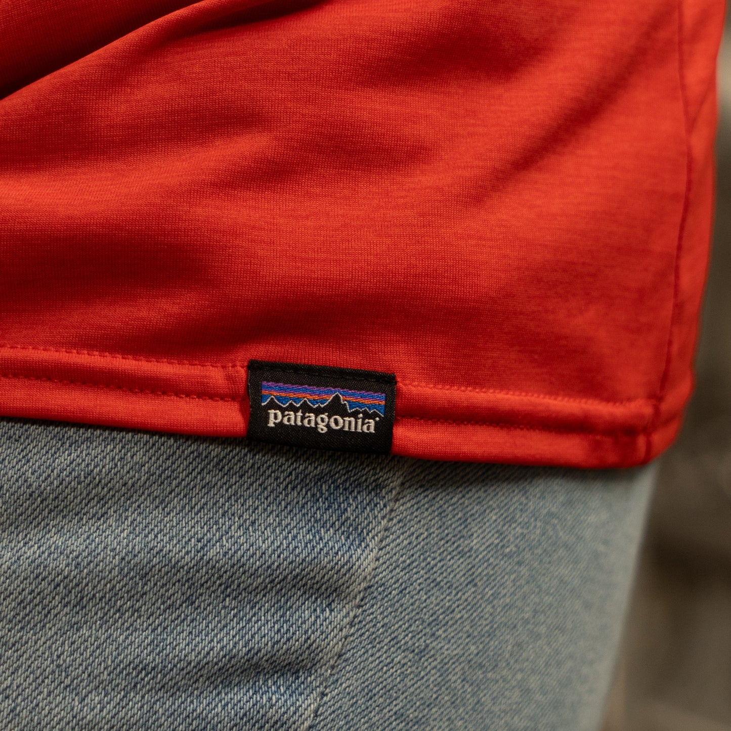 A close-up of the Patagonia W Red Long Sleeve Runner made with recycled polyester, featuring a visible Patagonia tag by the hem, paired with light blue denim jeans.