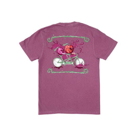Backside of Plum Bike Short Sleeve Tee. The backside of this shirt shows a purple plum and red apple riding a sage green and white tandem bike. Plum colored splashes sit at the wheels of the bike and background of the imagery with sage green lines that mimic tree branches border the top and bottom edges of the visual. 
