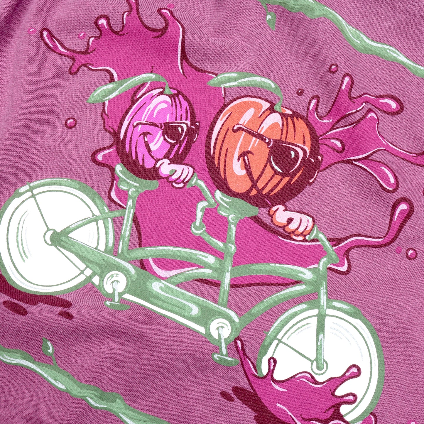Close up of the of Plum Bike Short Sleeve Tee design. The backside of this shirt shows a purple plum and red apple riding a sage green and white tandem bike. Plum-colored splashes sit at the wheels of the bike and background of the imagery with sage green lines that mimic tree branches bordering the top and bottom edges of the visual. 