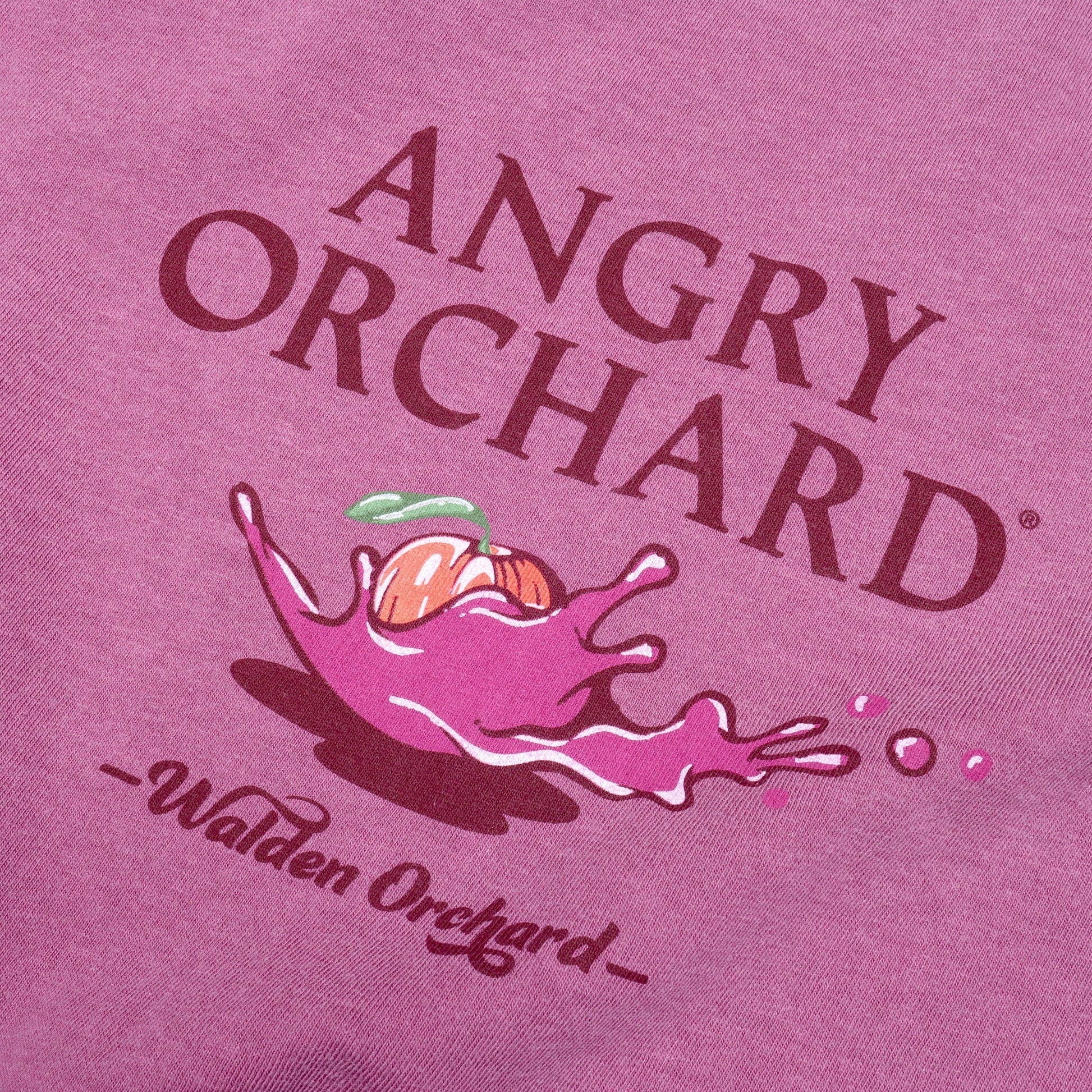 Close up of Plum Bike Short Sleeve Tee Design. Design is written in dark plum text reading from top to bottom, "Angry Orchard", then showing an Angry Orchard apple in motion, making a pink splash, "Walden Orchard" is written underneath this visual in a dark plum retro font. 