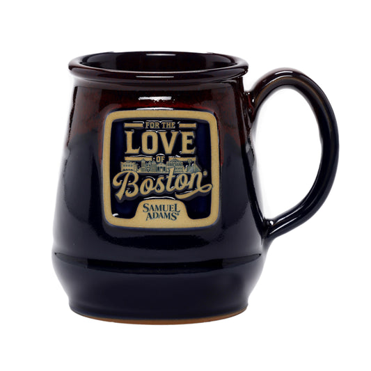 A navy ceramic mug with subtle red on the top with the classic Sam Adams "Love of Boston" logo on the front.