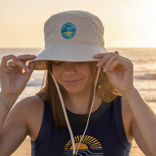Woman wearing a beige bucket hat with a logo on a beach at sunset