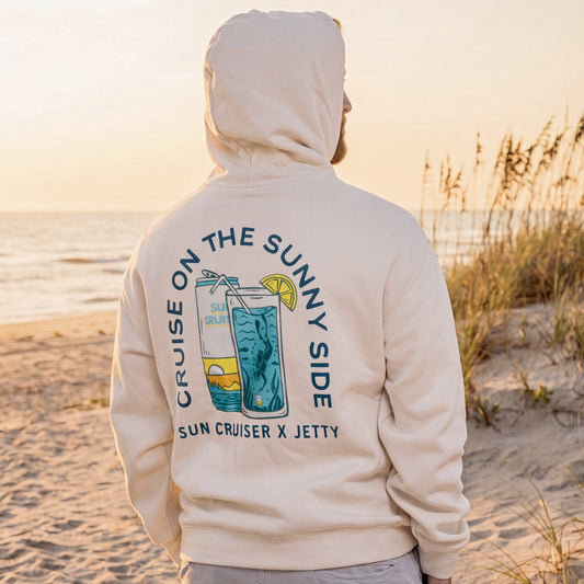 Person wearing a hoodie with a beach-themed design on a sandy beach at sunset.