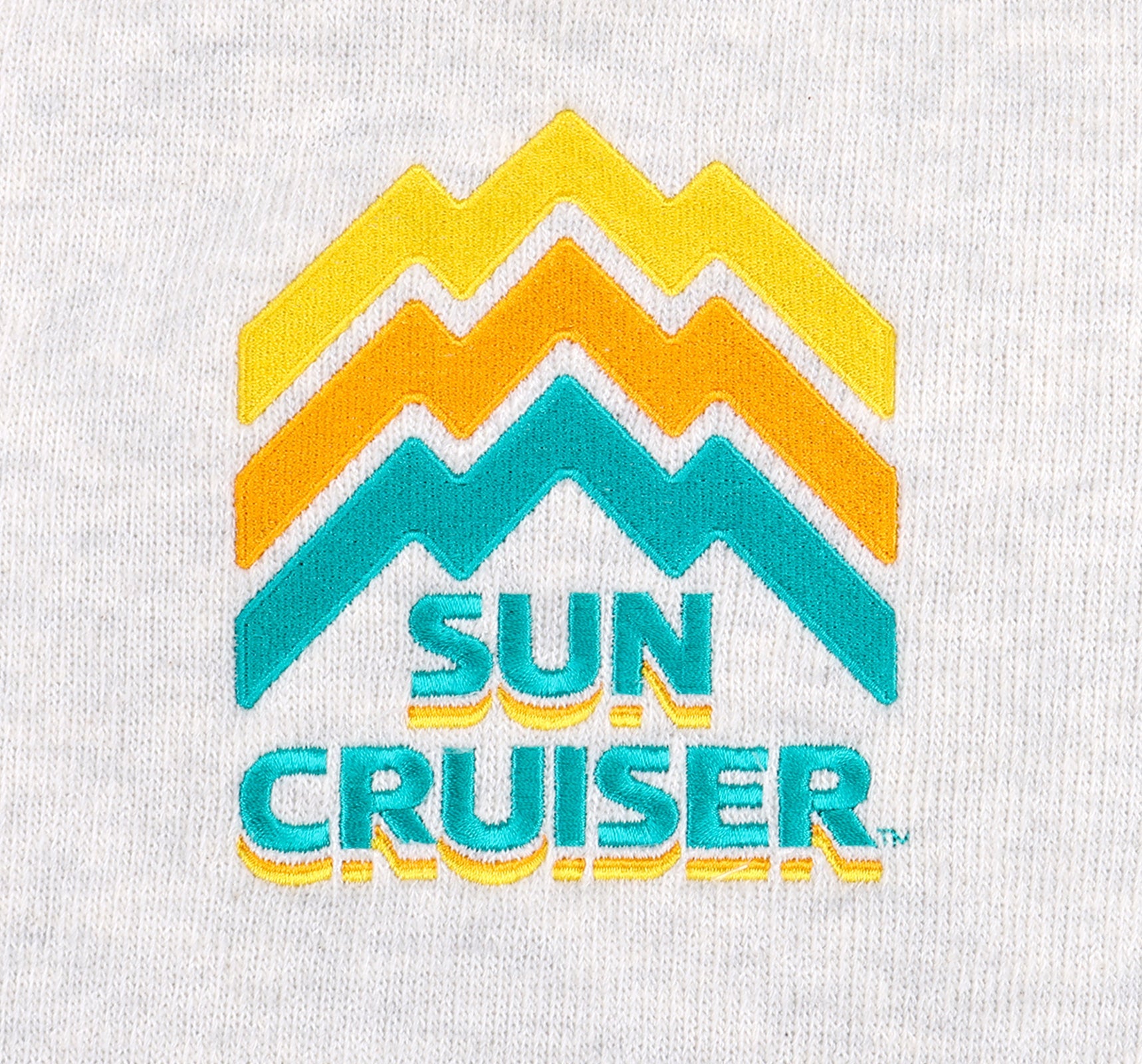 Close up of the centered embroidery logo on a Cream-colored Sun Cruiser Crewneck Sweatshirt. Line work on the logo is designed to look like a mountain range, in classic sun cruiser colors cyan, orange, and yellow