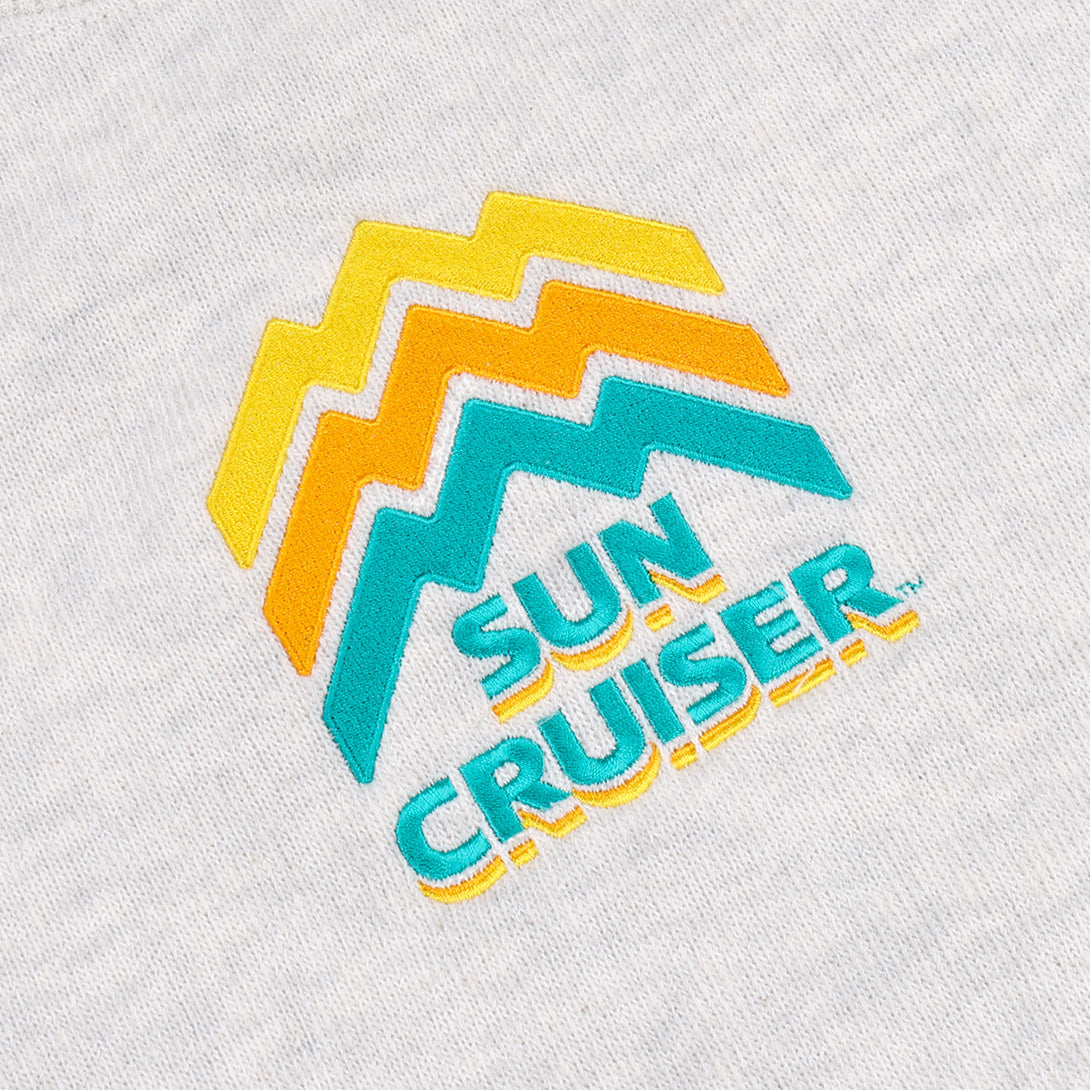Close up of the centered embroidery logo on a Cream-colored Sun Cruiser Crewneck Sweatshirt. Line work on the logo is designed to look like a mountain range, in classic sun cruiser colors cyan, orange, and yellow