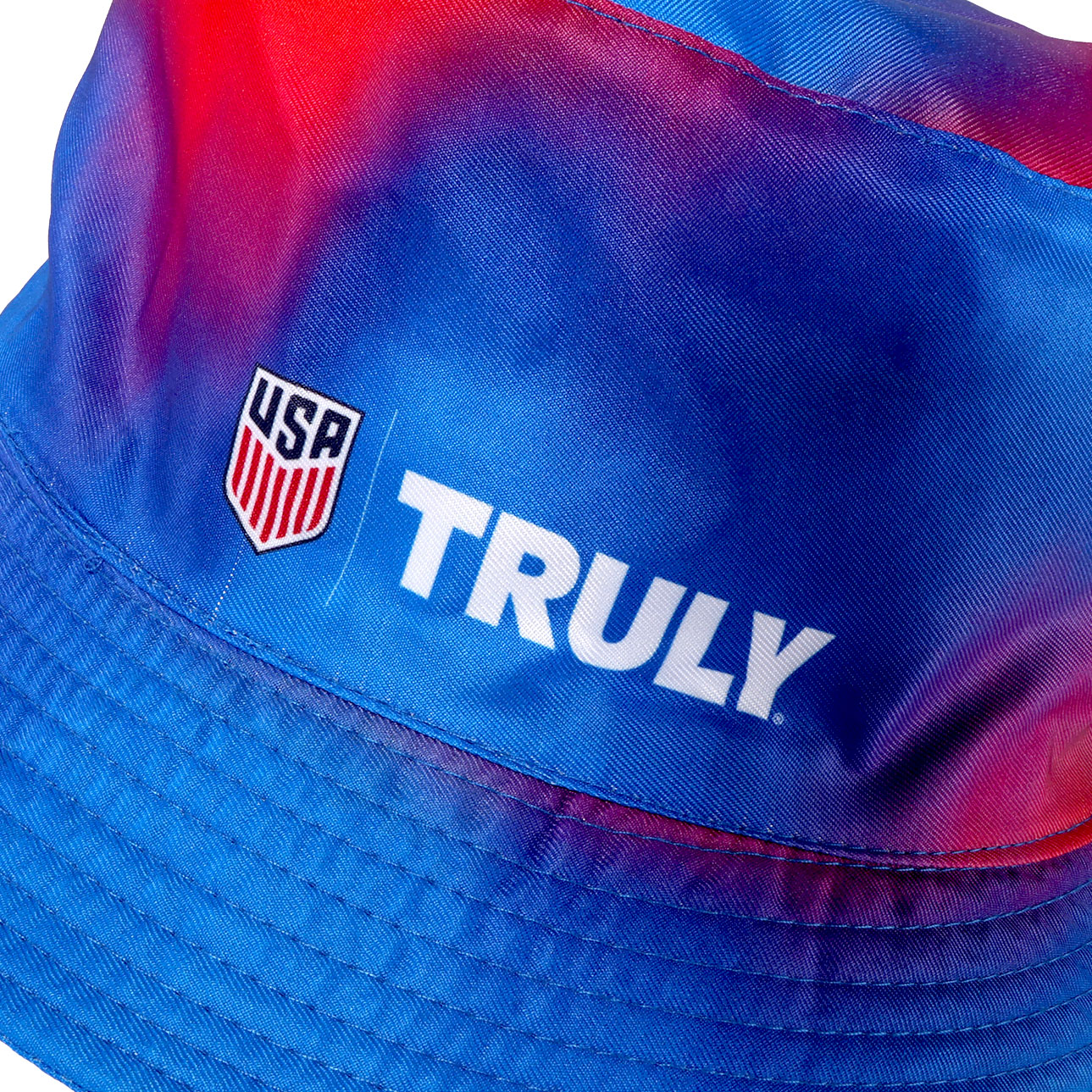 Close up of USA logo and Truly logo in white text on a red and blue tie dye bucket hat 