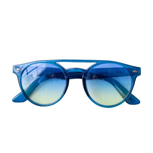 Front view of Samuel Adams sunglasses with transparent blue frame, rounded retro lens shape, yellow‑to‑blue gradient lenses, molded nose bridge, and metallic rivet accents at the corners