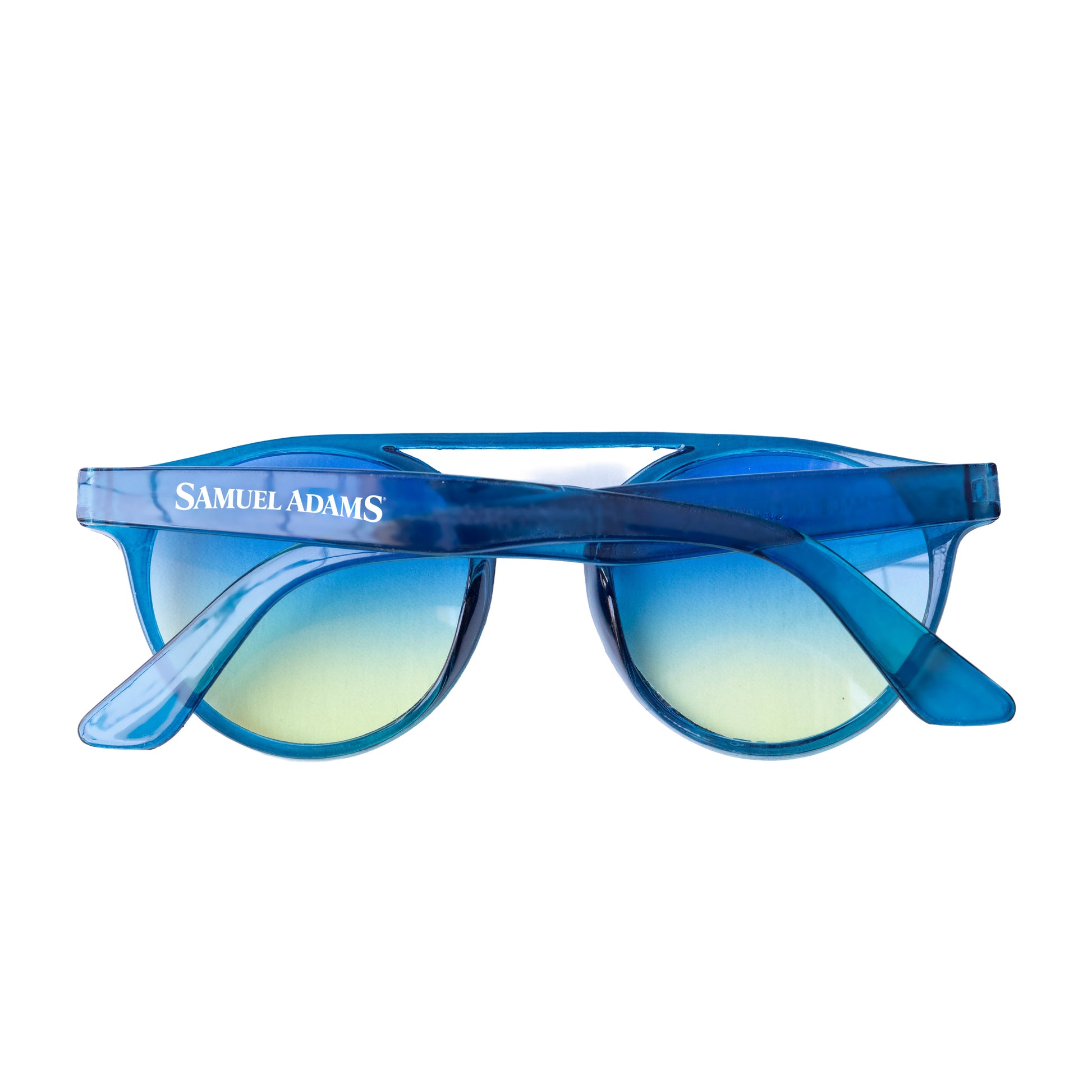 Folded Samuel Adams sunglasses with translucent blue frame, gradient blue and yellow lenses, and white “Samuel Adams” text printed on the outer arm