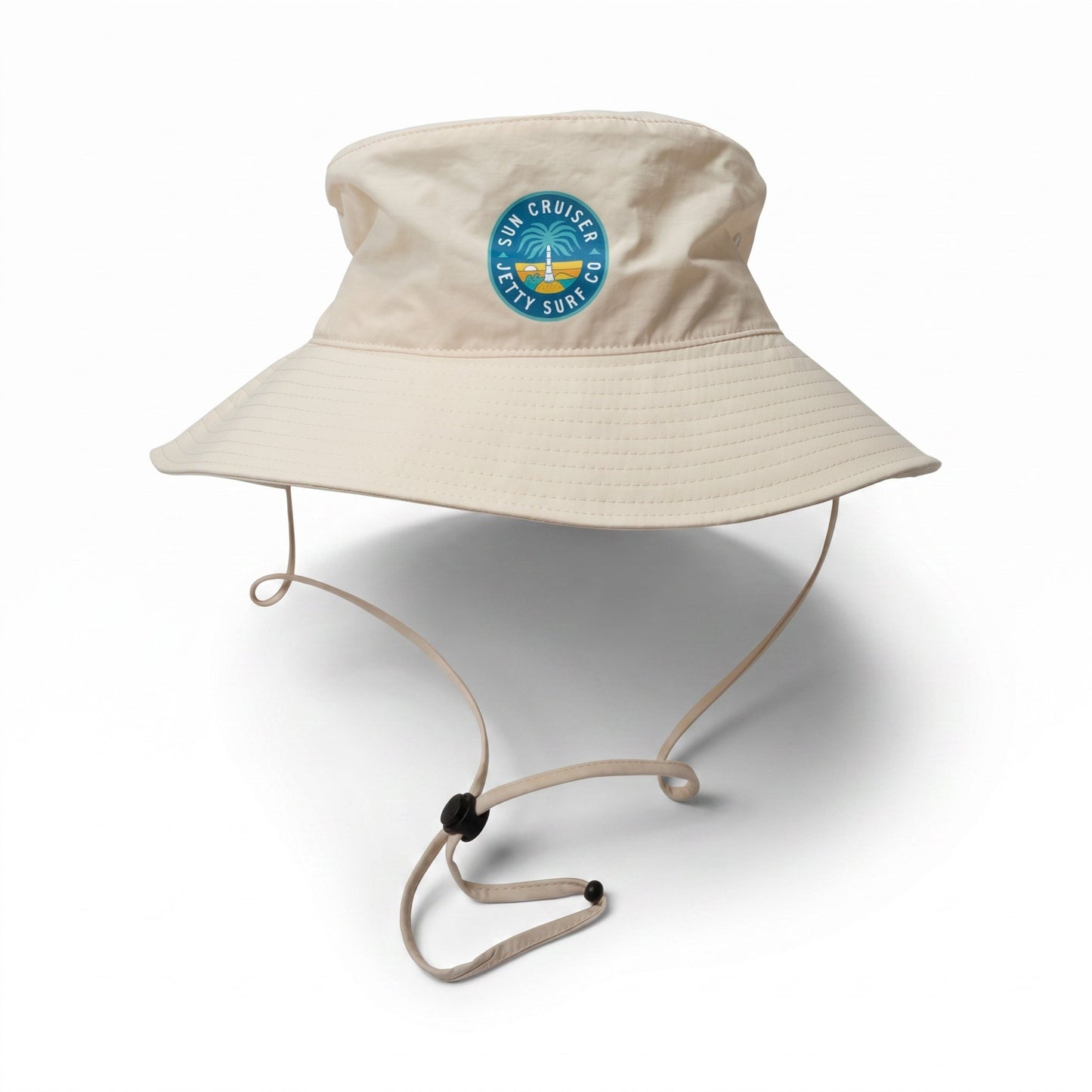 A beige wide-brim bucket hat with an adjustable chin strap, featuring a circular blue and green 'Sun Cruiser x Jetty Surf co' logo  on the front, set against a plain white background.