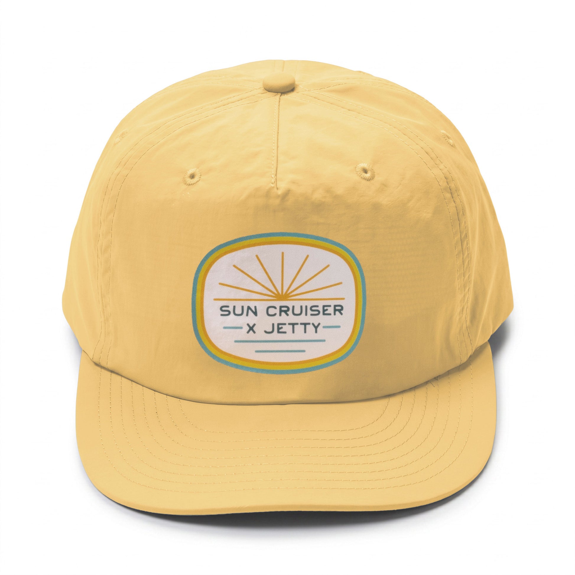 A yellow baseball cap featuring a circular embroidered patch on the front that reads 'SUN CRUISER X JETTY' with a sunburst design.