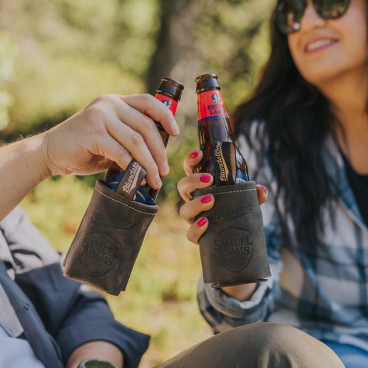 Two people cheering two samuel adams bottles in Samuel Adams x BLUNDSTONE Leather Can and Bottle Coolers