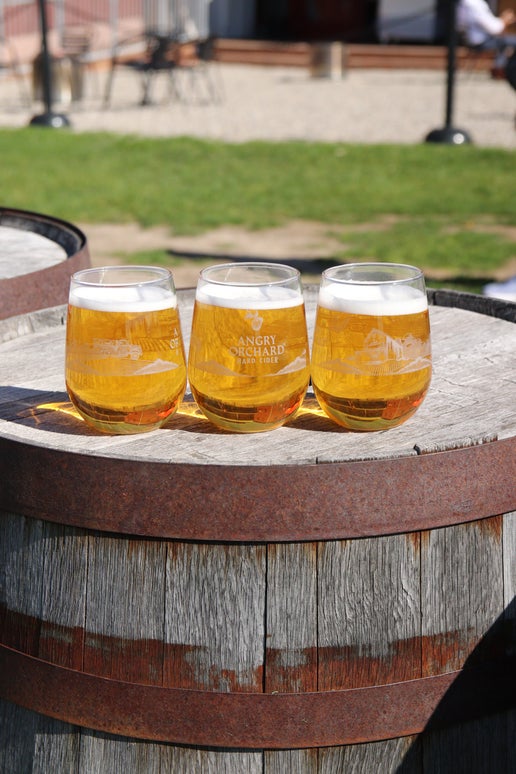 On one side of this glass is an apple and under it the writing "Angry Orchard Hard Cider". Under the writing is the beginning of a silhouette of the Angry Orchard, which continues to the next side. The other side of the glass as a full white silhouette of the Angry Orchard. 