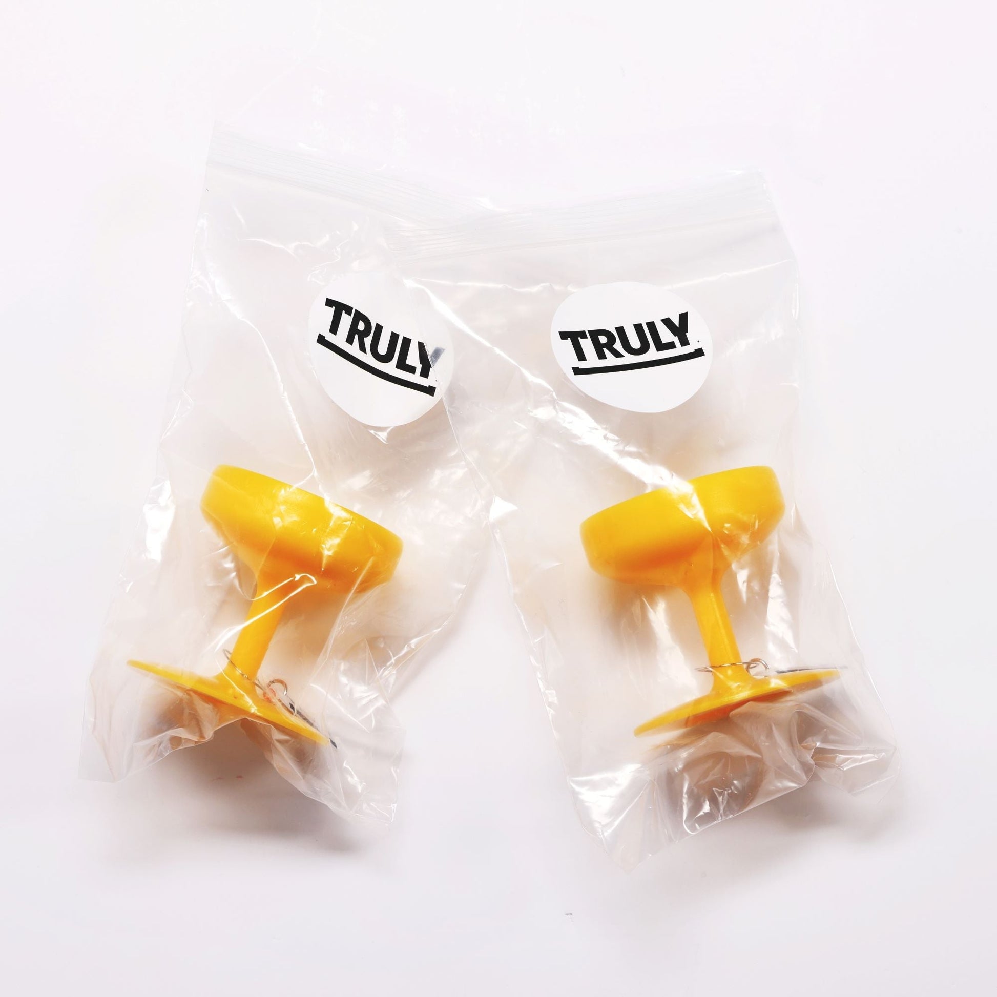 Two yellow plastic bases shaped like the bottom of stemmed glasses, packaged separately in clear plastic bags with a "TRULY" logo sticker on each, against a white background.