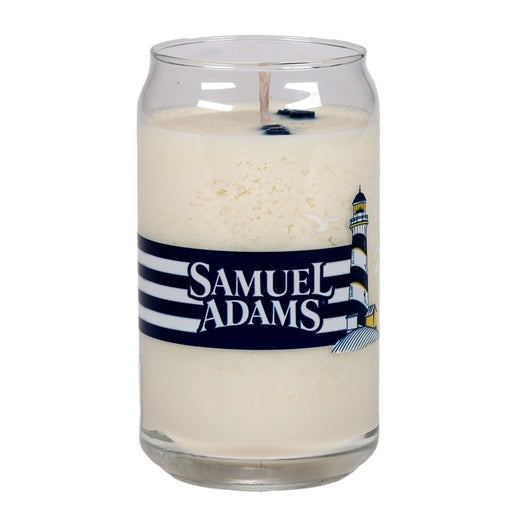 Candle with Black, white, and yellow Samuel Adams logo and a light house design. Black and white stripes wrap the middle of the candle connecting to a Samuel Adams hoist a beer logo to form a near 360 design.