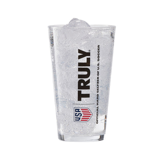 Clear pint glass filled with ice and a carbonated beverage, featuring vertical black “TRULY” branding and a red‑and‑blue shield‑style USA graphic. Beneath in smaller text is "Official Hard Seltzer of U.S. Soccer". Fine bubbles are visible throughout the drink, and the glass has a clean, modern shape suitable for beverages or barware.