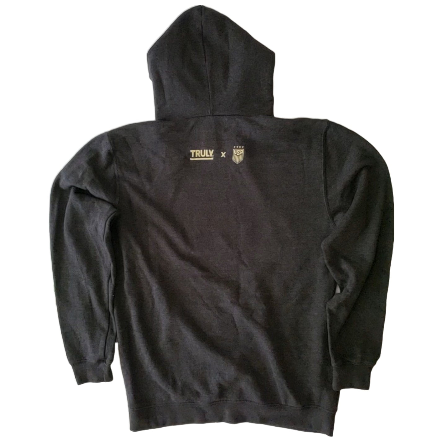 A dark gray hooded sweatshirt, viewed from the back. Near the top center of the back, there are two logos in a light, possibly gold or beige, color. On the left is the word "TRULY" with a horizontal line underneath it. To the right of "TRULY" is an "X" and then a emblem with "USA" and what appears to be a crest or shield design. The sweatshirt has long sleeves and a hood.