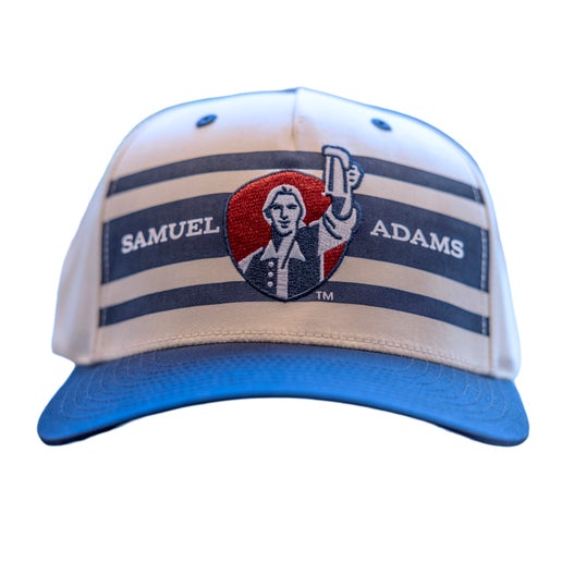 Front view of hat features a blue front panel. Base of hat is white with blue stripes across the front and writing "Samuel Adams" on the middle stripe. Centered is Sam Adams hoisting a beer on a red shield.