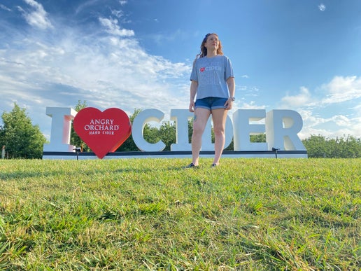 Front of gray tee displays five rows of writing "I Heart Cider". Heart is an actual heart and inside it is writing "Angry Orchard Hard Cider". Second row of writing is bolded with a red heart. 