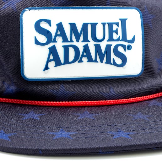 A navy trucker hat with red rope piping and a white Samuel Adams patch on the front. Reveals blue stars when wet.