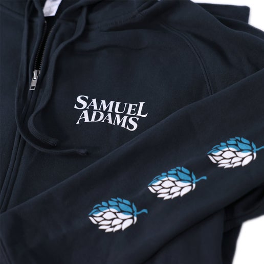 Close up of white Samuel Adams logo on the left chest of navy hoodie and three blue/white ombre hops designed on both sleeves.