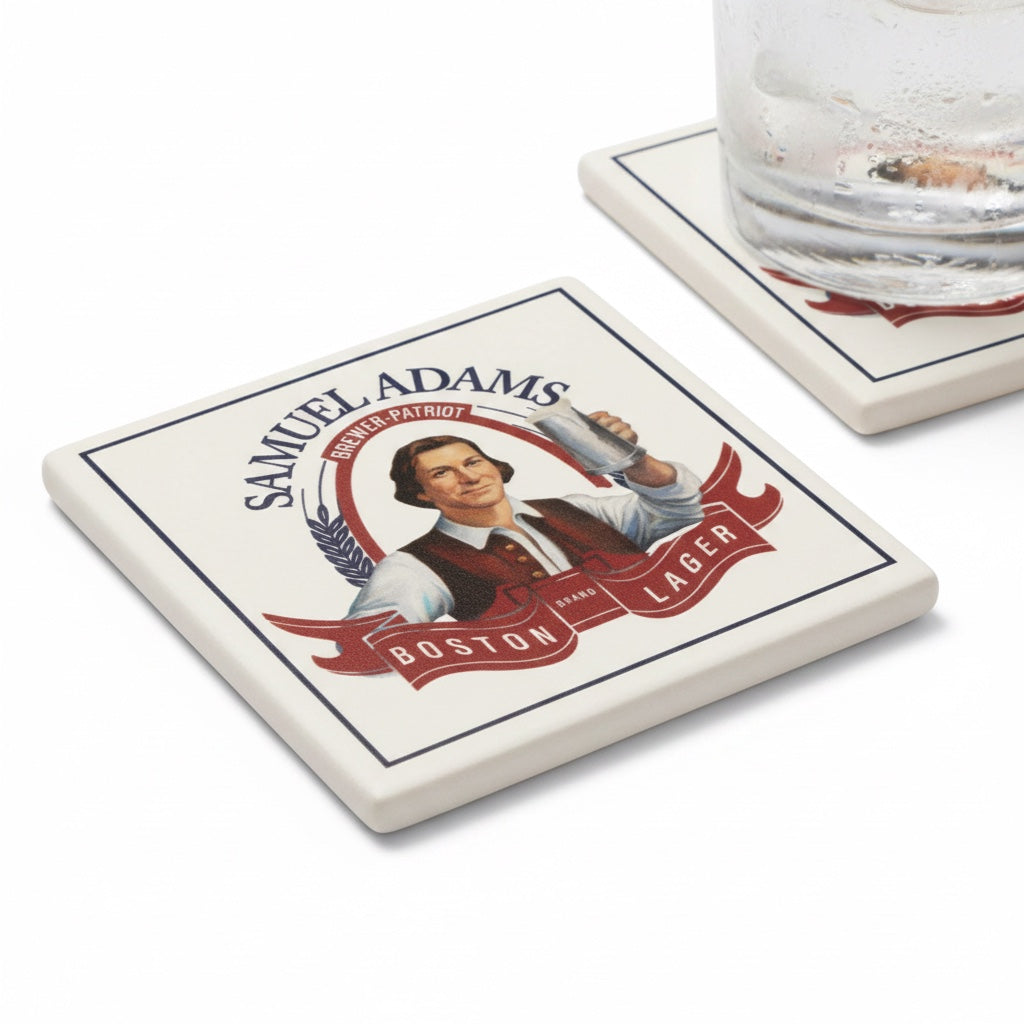 An angled view of a coaster, with curved Sam Adams text at the top, "Brewer Patriot" underneath the top text. Featuring a colonial dressed person raising a stein. "Boston Lager" is written in white within in a flag shape at the bottom. 